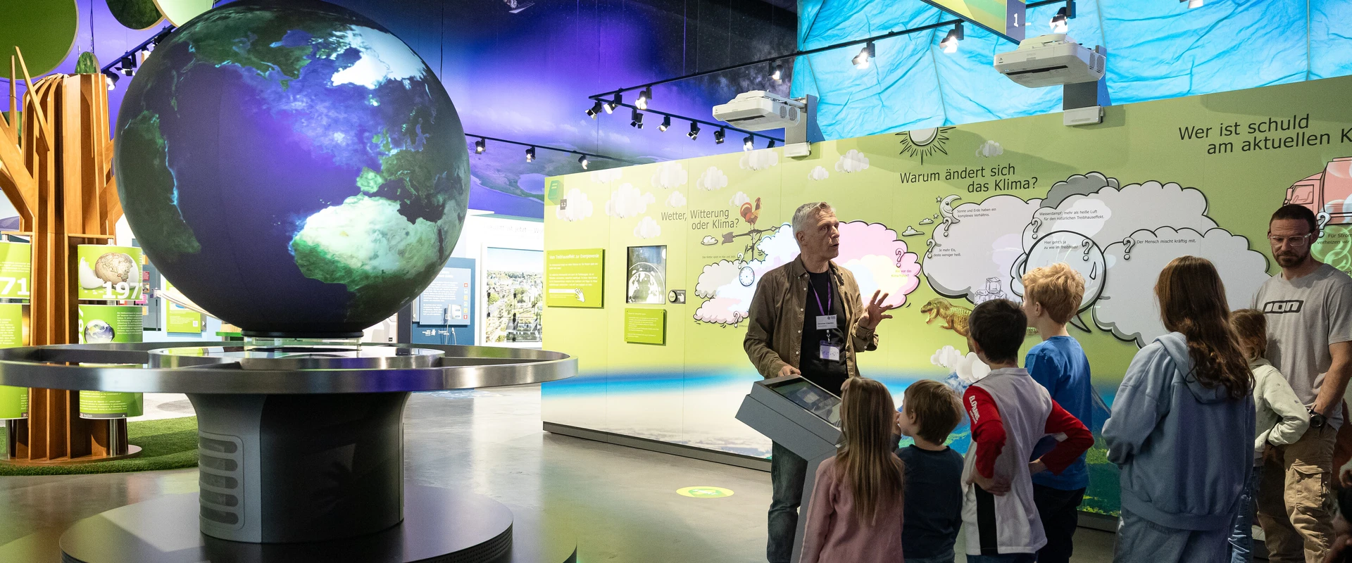 Familie mit Besucherbetreuer bei F&uuml;hrung am interaktiven Globus.